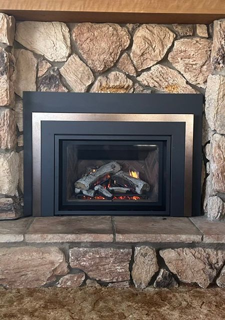 Stone fireplace with a black gas insert and glowing embers in a rustic interior