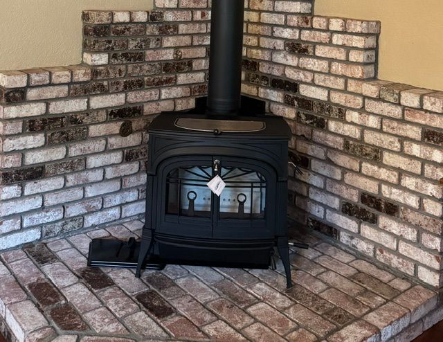 Black wood stove in a brick corner alcove with a stovepipe and brick hearth floor.