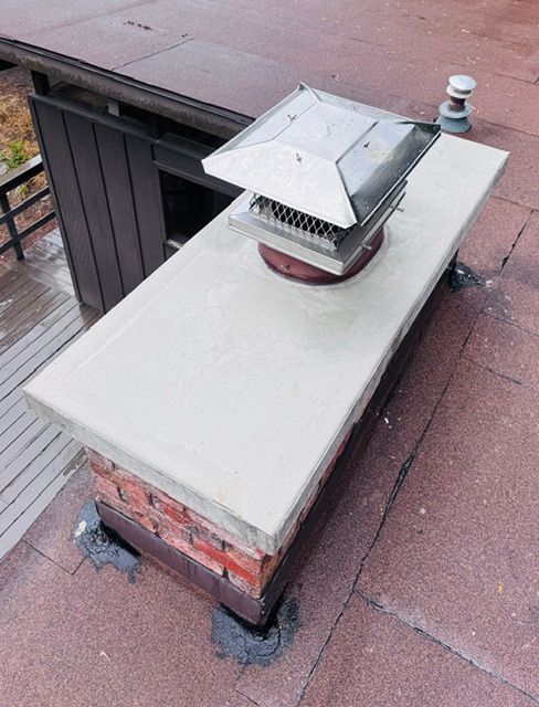 Rooftop vent pipe with white metal chimney cap on a brick and concrete base