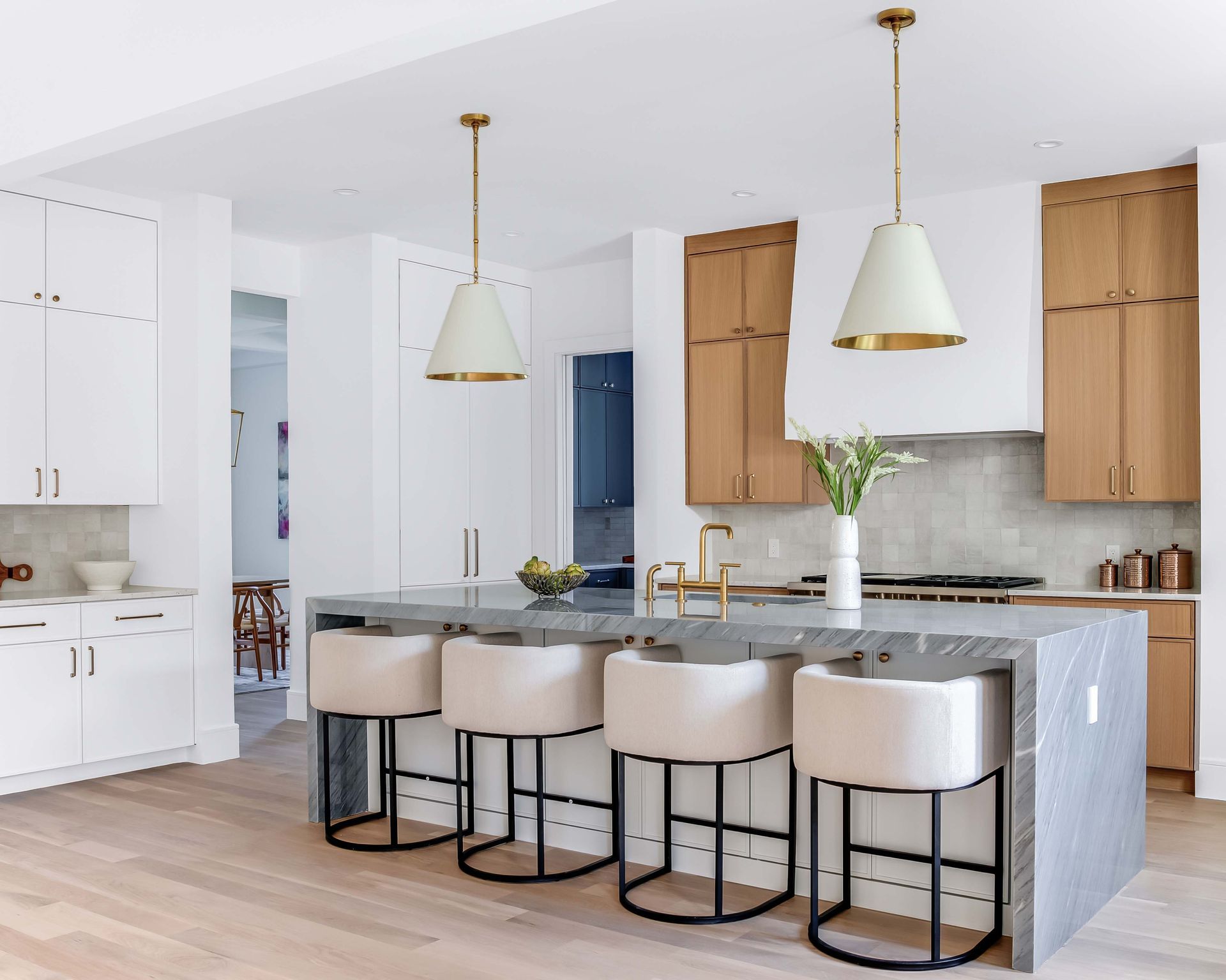 Modern kitchen with a gray island, white cabinets, wooden cabinets, and pendant lights.