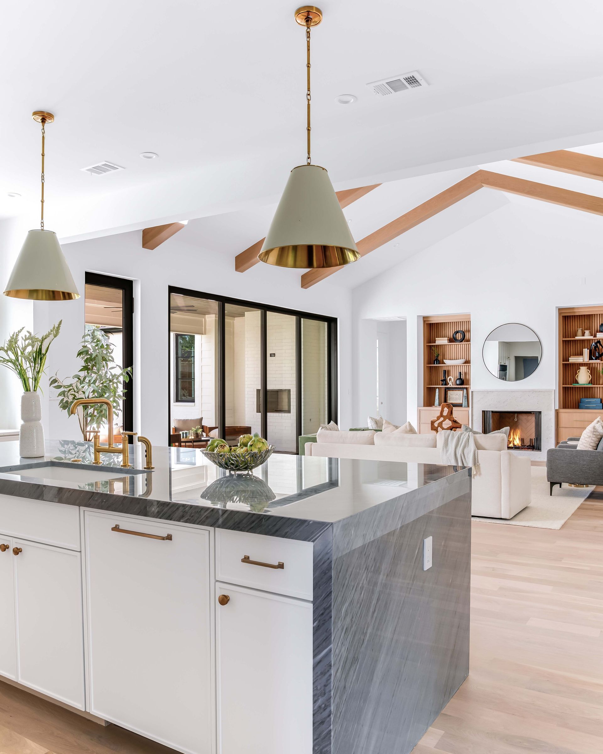 Kitchen island with white cabinets, gray countertop, and gold pendant lights, open to living area.