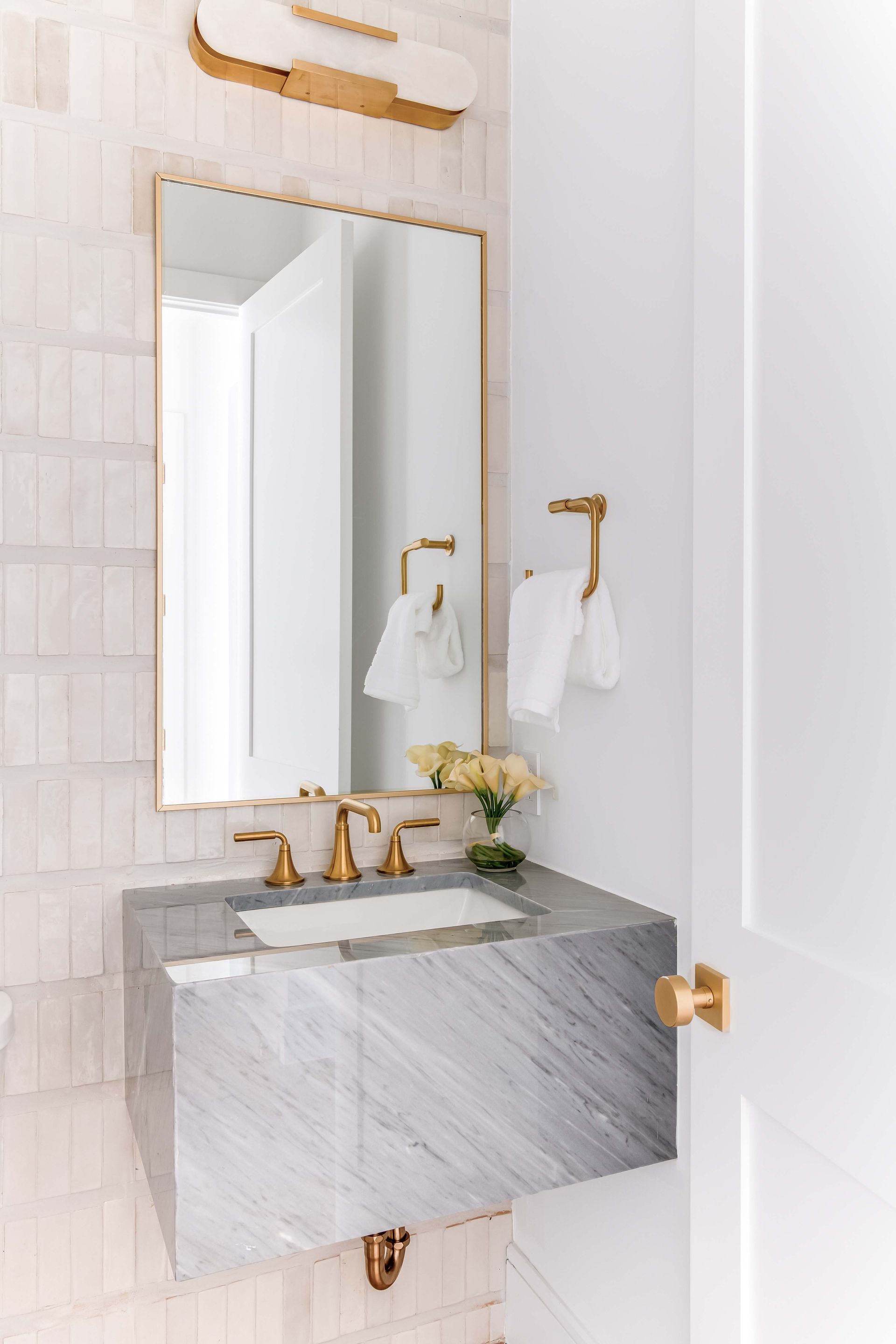 A small, modern bathroom with a marble vanity, gold fixtures, and a rectangular mirror.