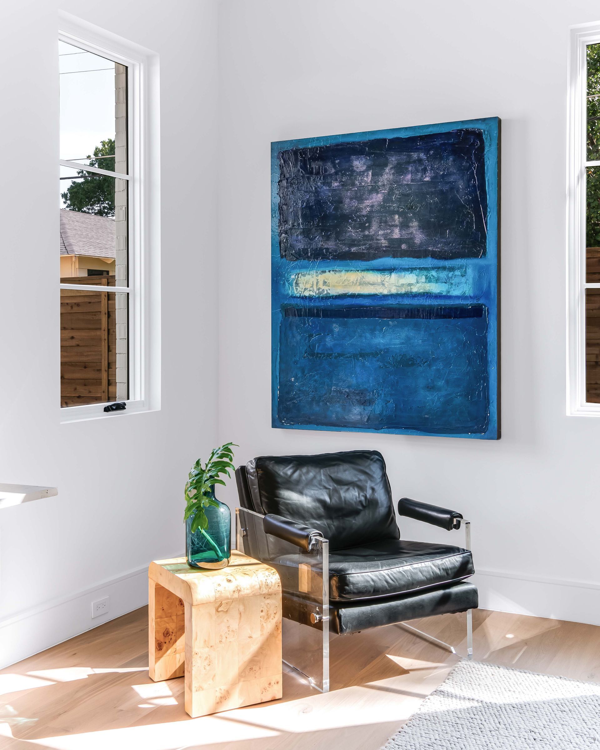 Corner room with blue painting, black chair, small wooden table, and windows.