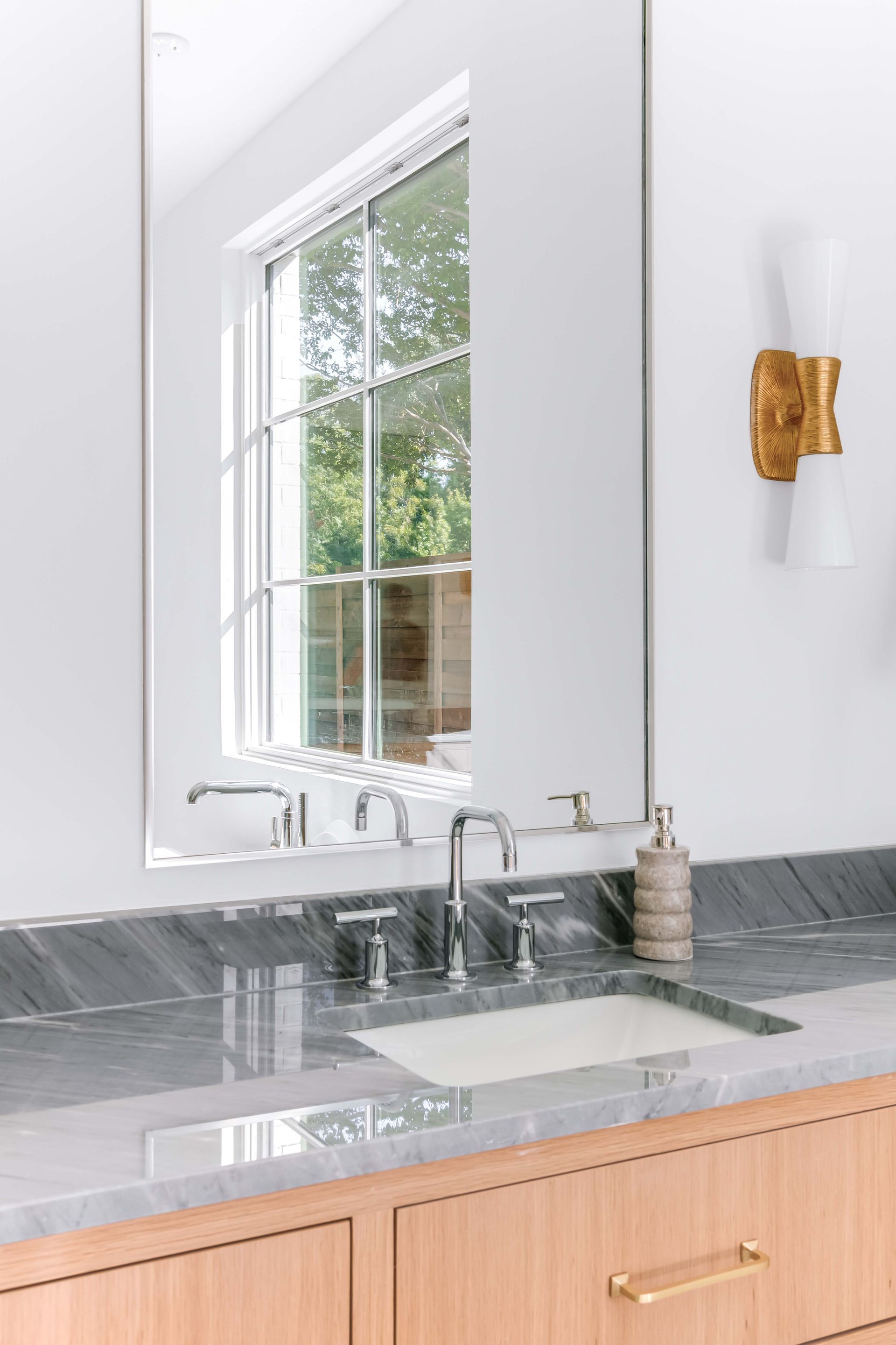 Bathroom with mirror over sink, window, and gold sconce.