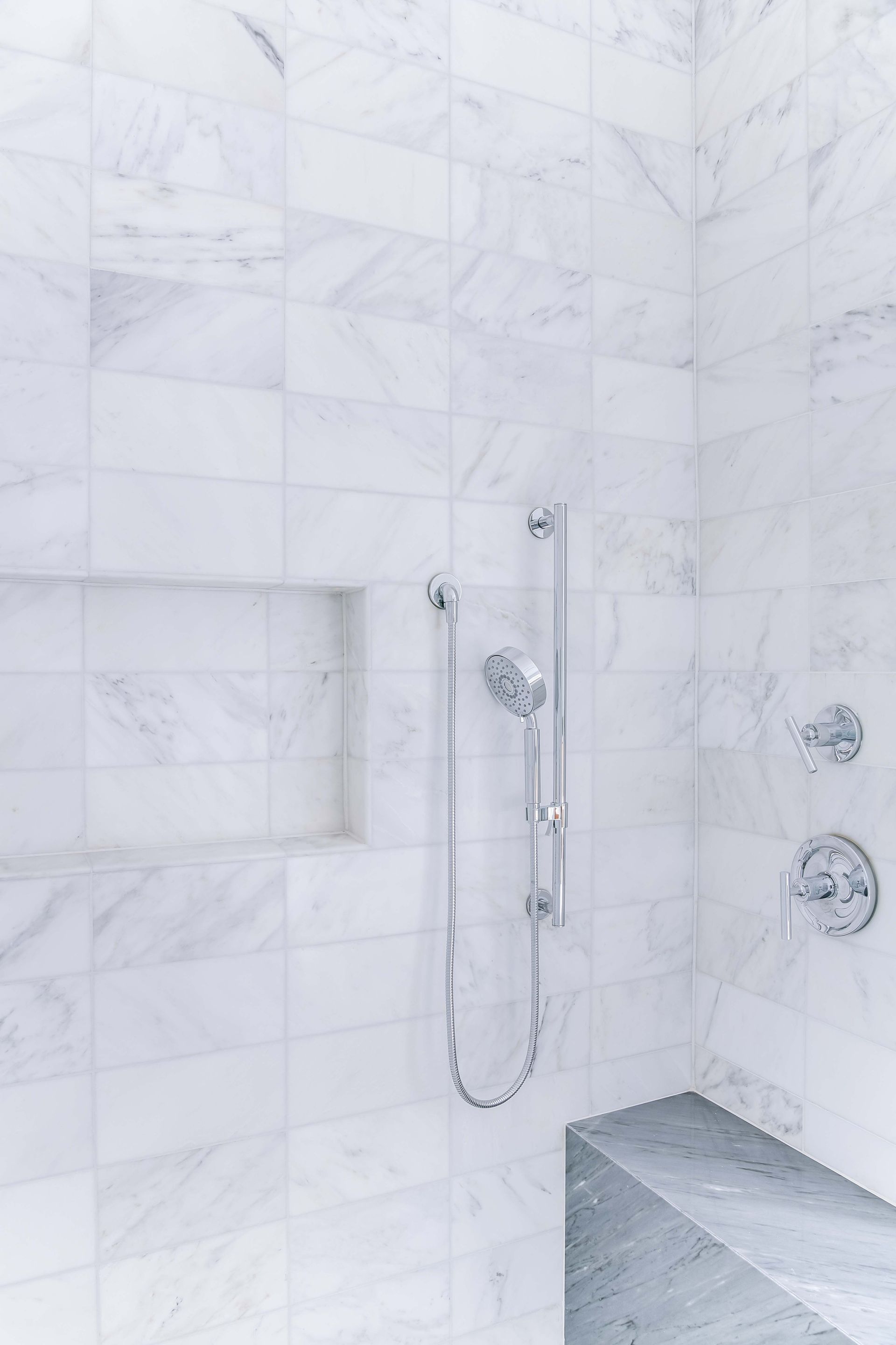White marble shower with a handheld shower head and built-in bench.