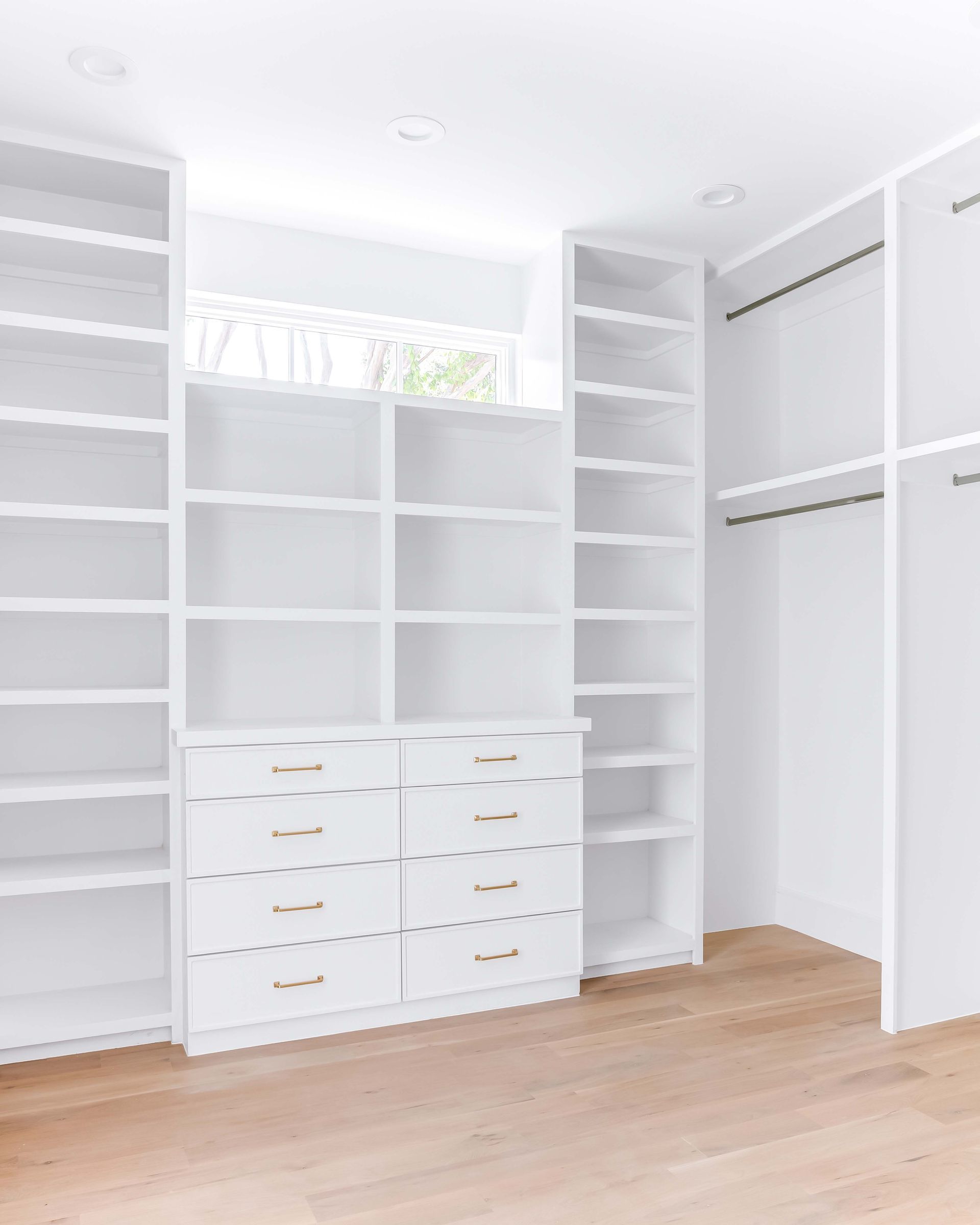 White custom closet with shelves, drawers, and hanging rods; light wood floor.