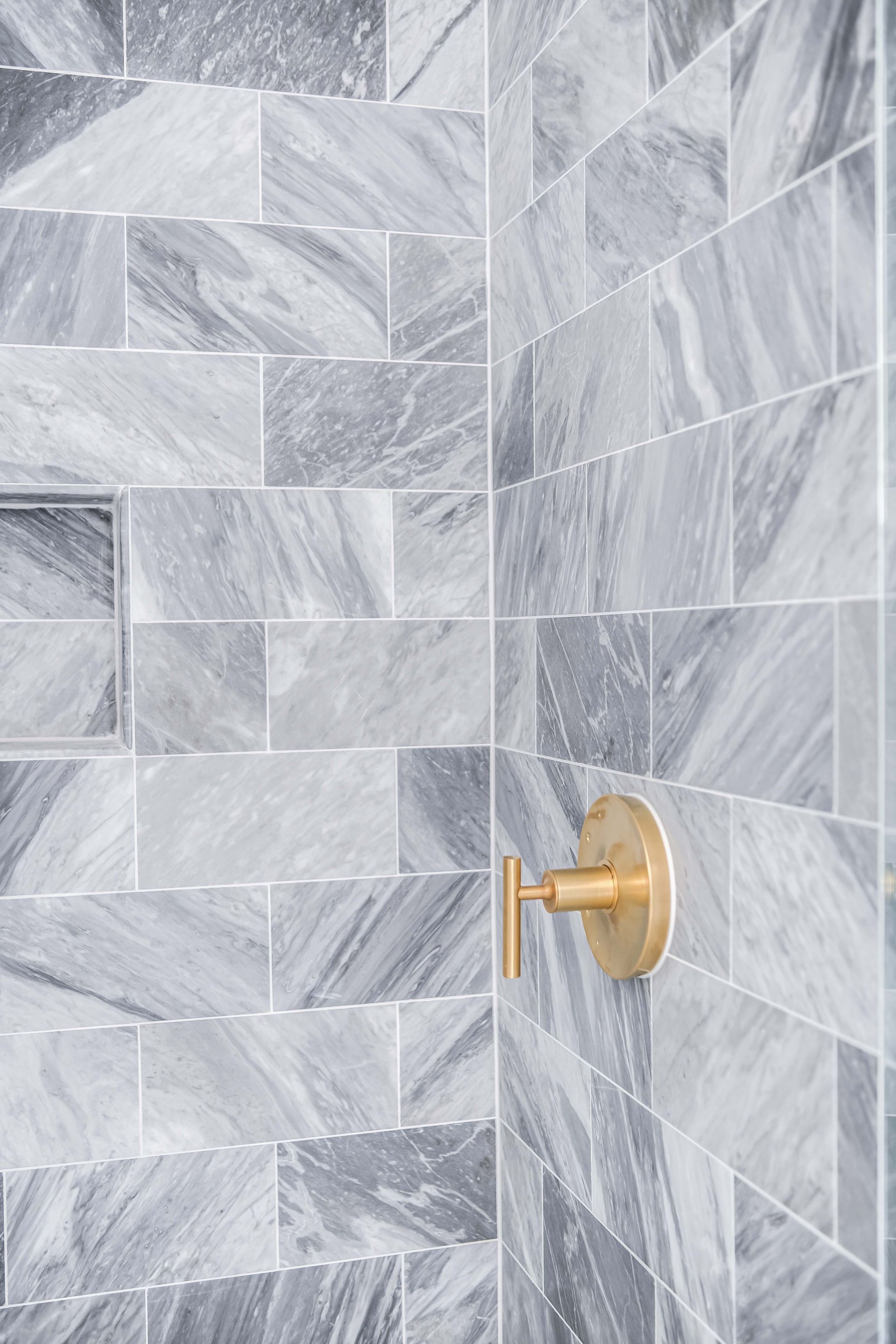 Gray marble-tiled shower with gold faucet handle.