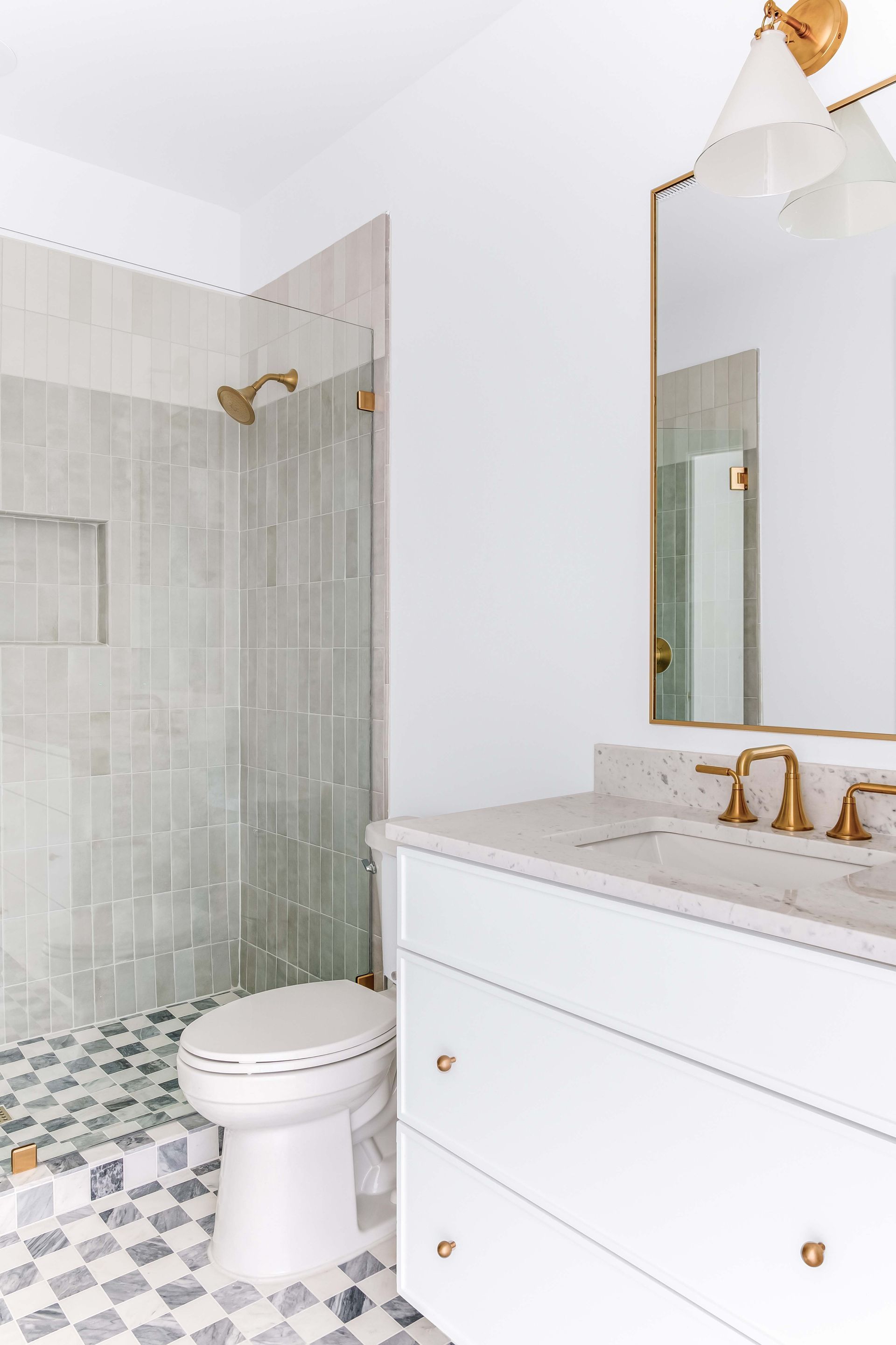 Bathroom with white vanity, gold fixtures, checkered floor, and tiled shower.