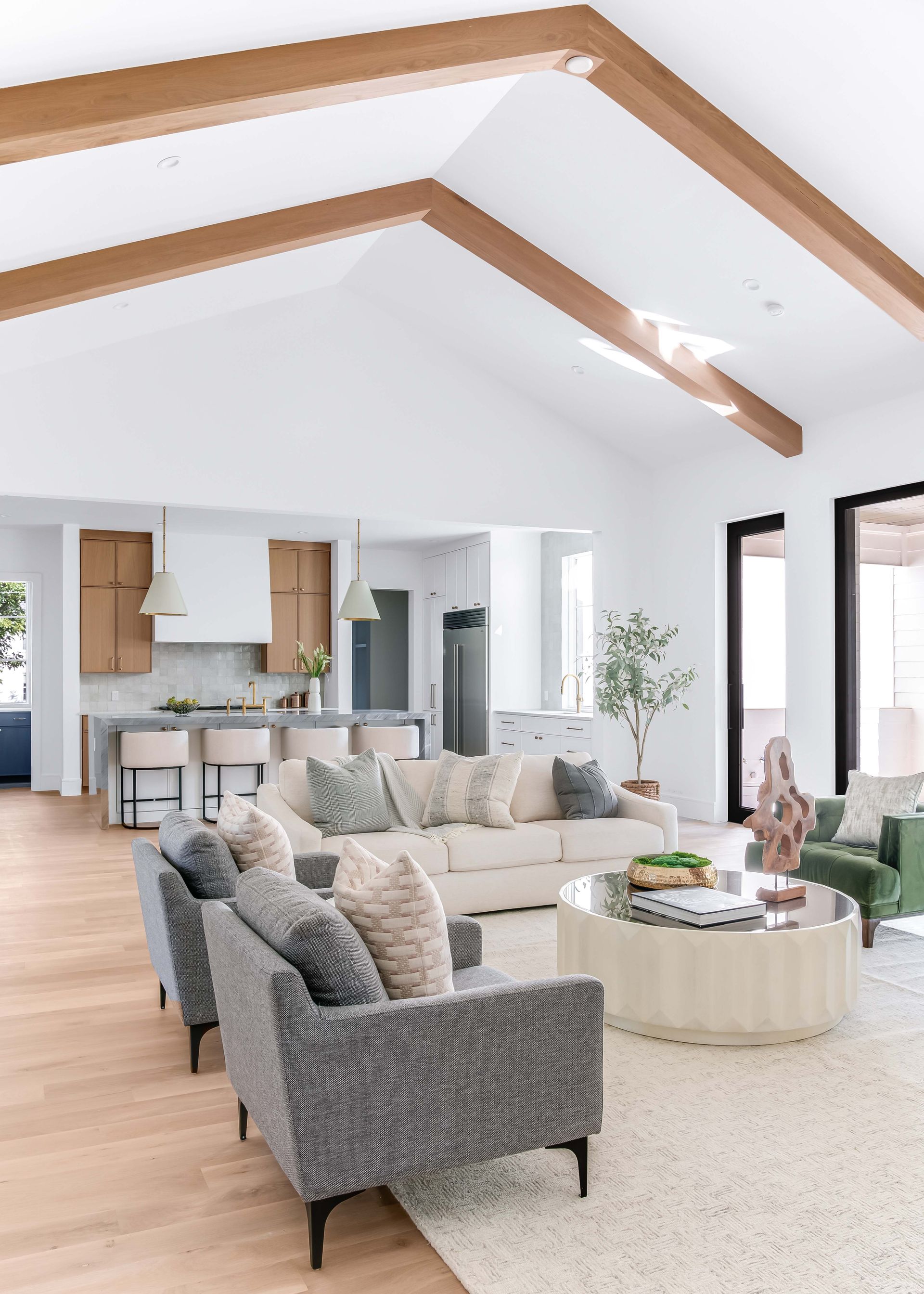 Spacious living room with vaulted ceiling, wood beams, and open kitchen. Neutral color scheme.