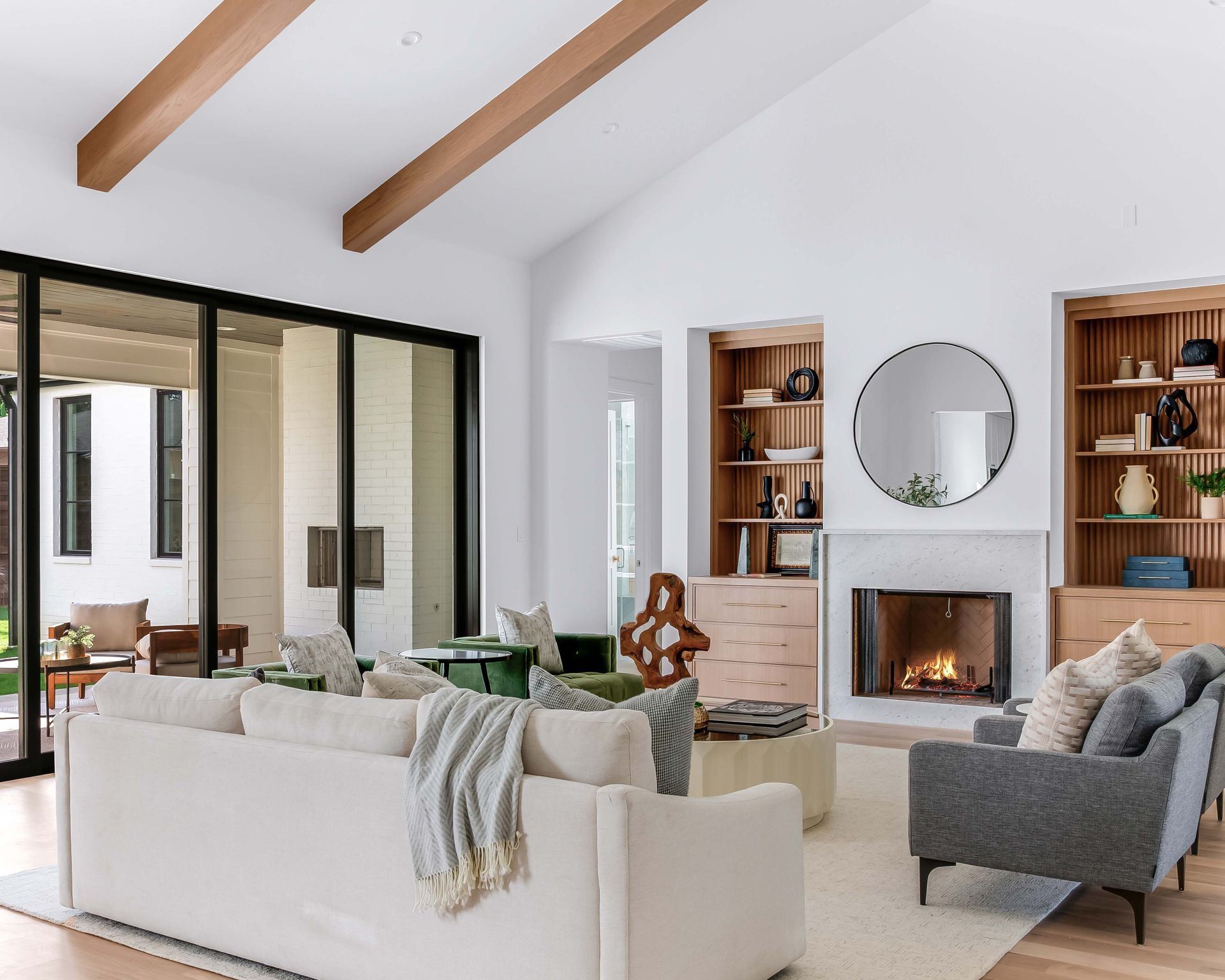 Modern living room with white walls, wooden beams, fireplace, and sliding glass doors.
