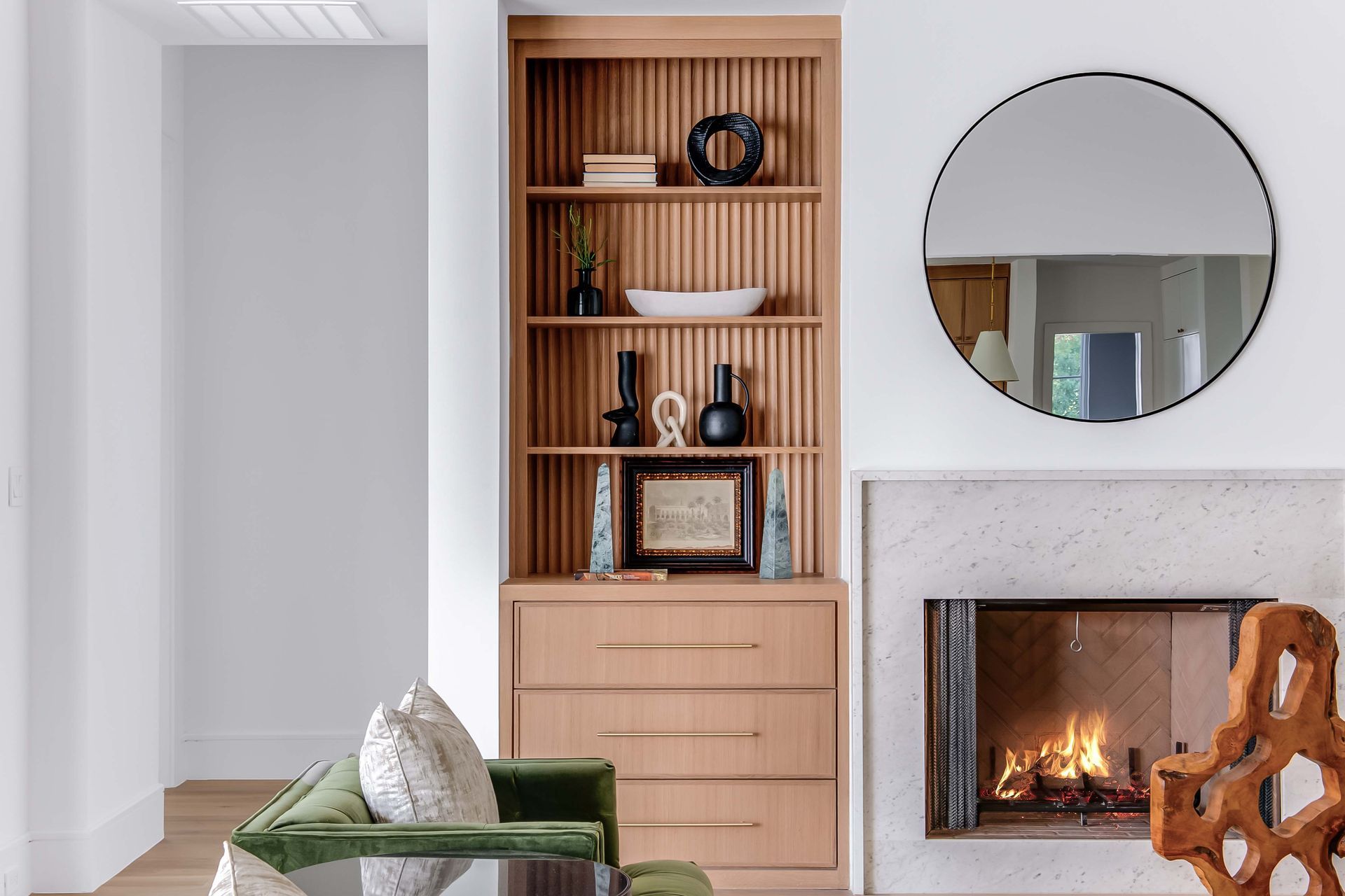 Living room with built-in bookshelf, fireplace, round mirror, and green velvet armchair.