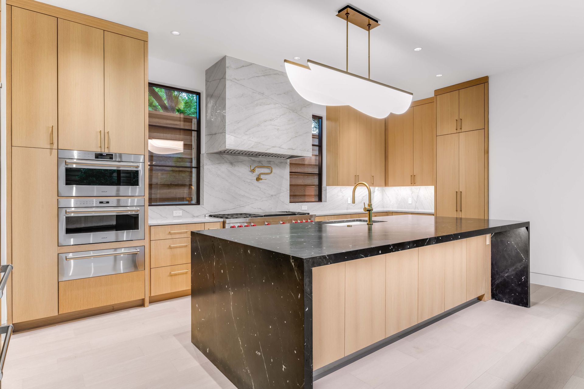 Modern kitchen with wood cabinets, black island, and marble accents.
