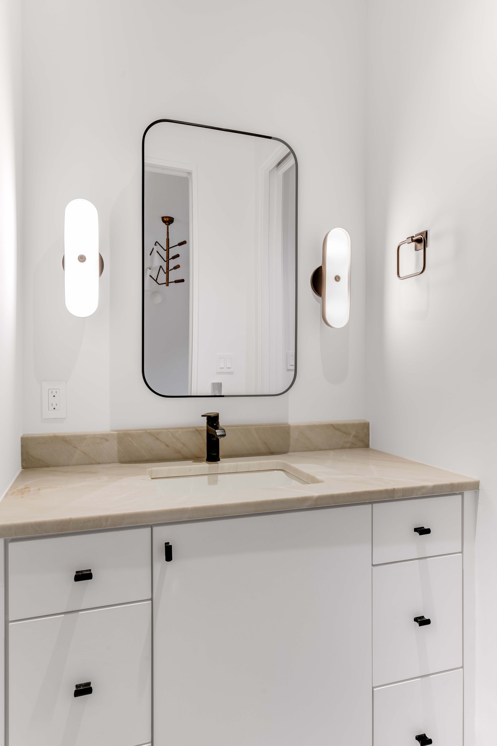 White bathroom vanity with black faucet and hardware, mirror, and sconces on white walls.