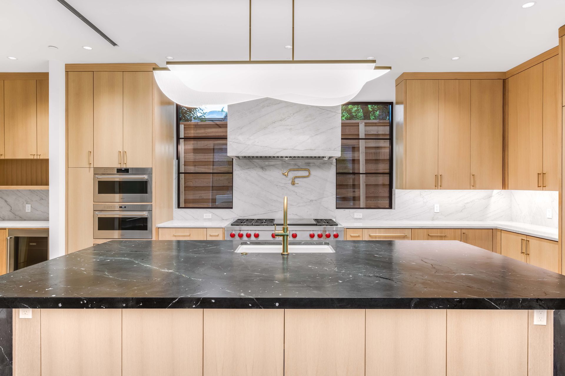 Modern kitchen with black island, light wood cabinets, and marble backsplash.