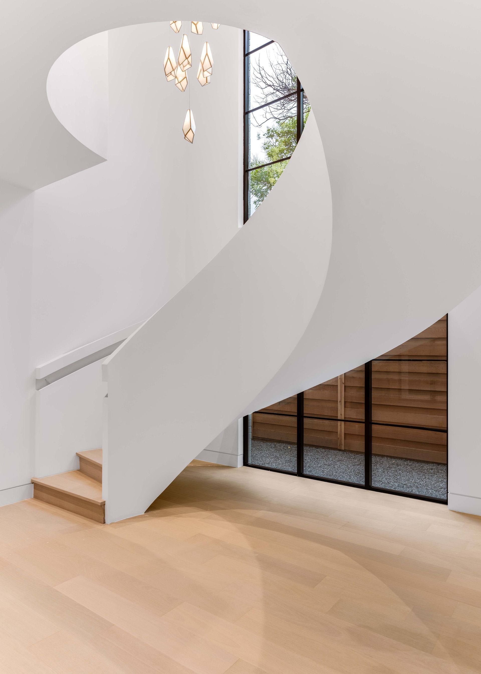 White spiral staircase with wood steps, light wood floor. Large windows, modern chandelier.