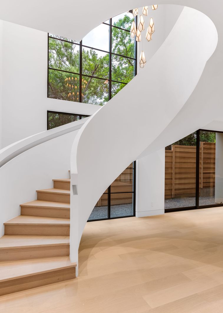 Hallway with large black-framed windows, wood flooring, and gold pendant lights.