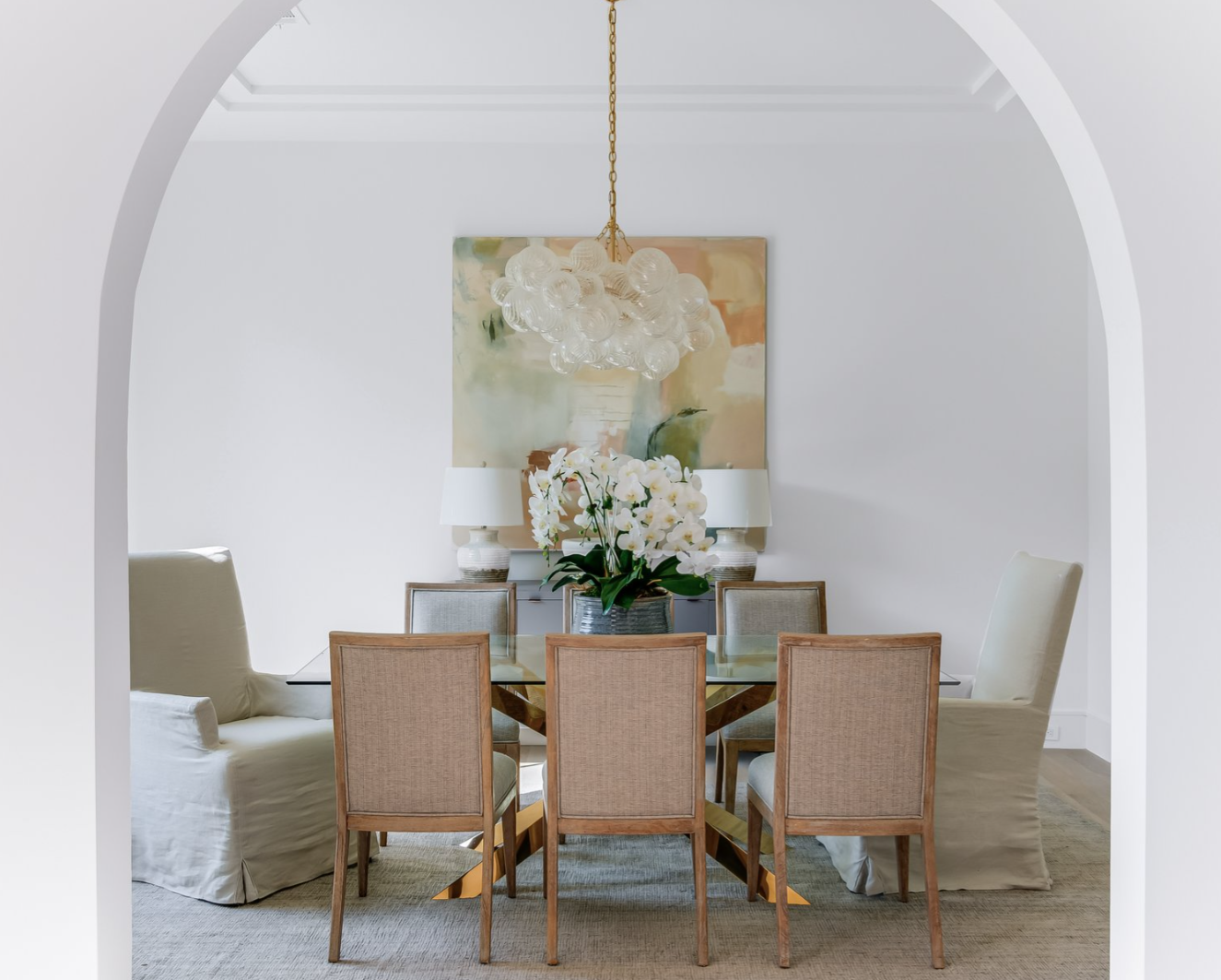 Dining room with table, chairs, and floral arrangement; viewed through a white archway.