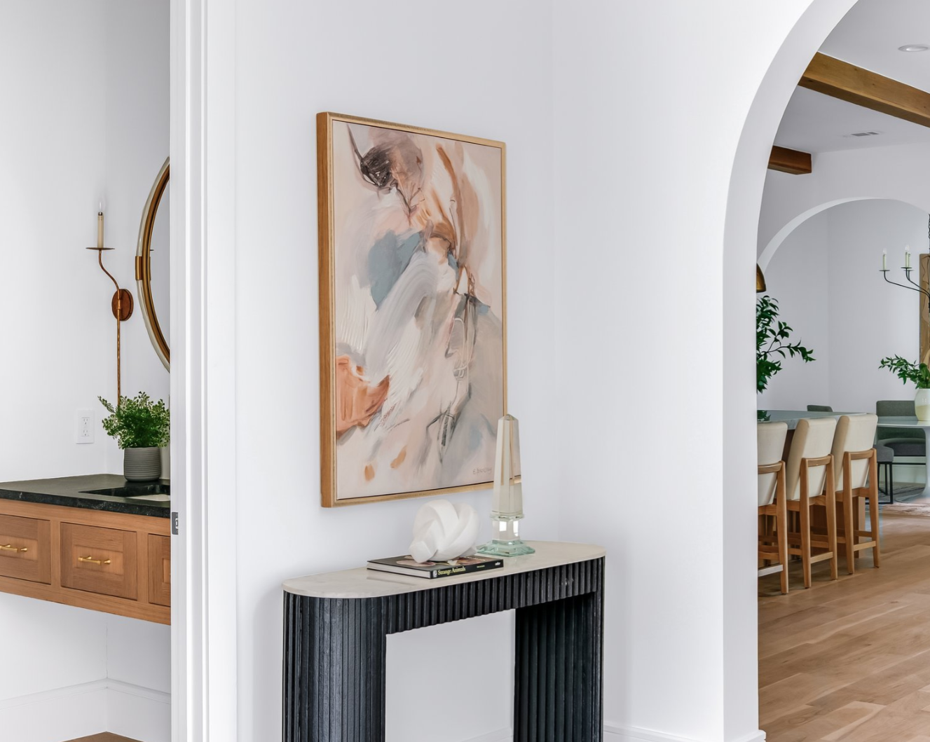 Hallway with console table and abstract art, archway to dining area with a wooden table.