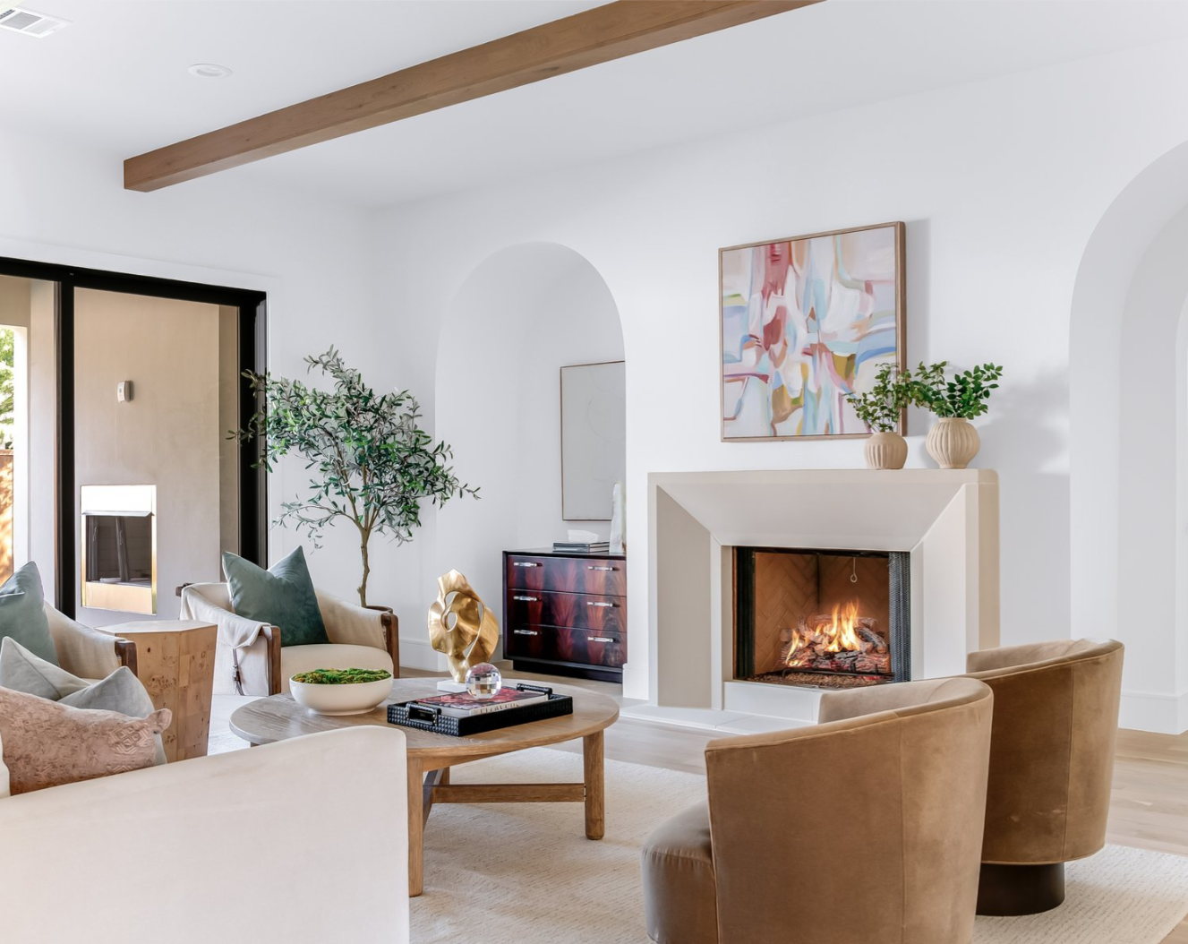 Living room with fireplace, arched doorways, white walls, tan furniture, and wooden accents.