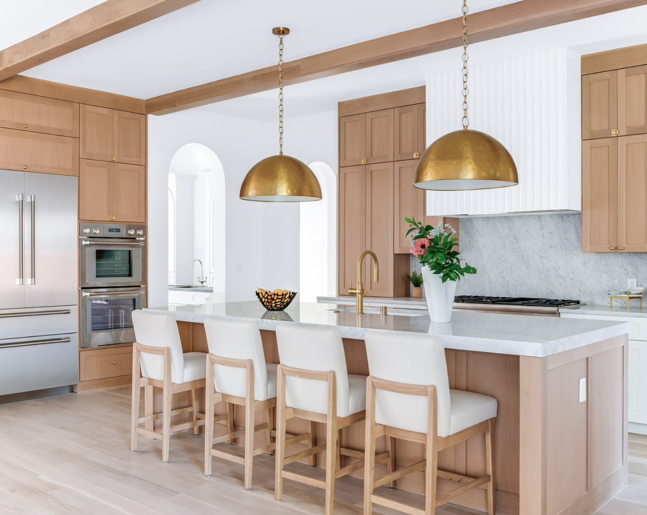 Elegant kitchen with light wood cabinets, gold pendant lights, and a central island with bar stools.