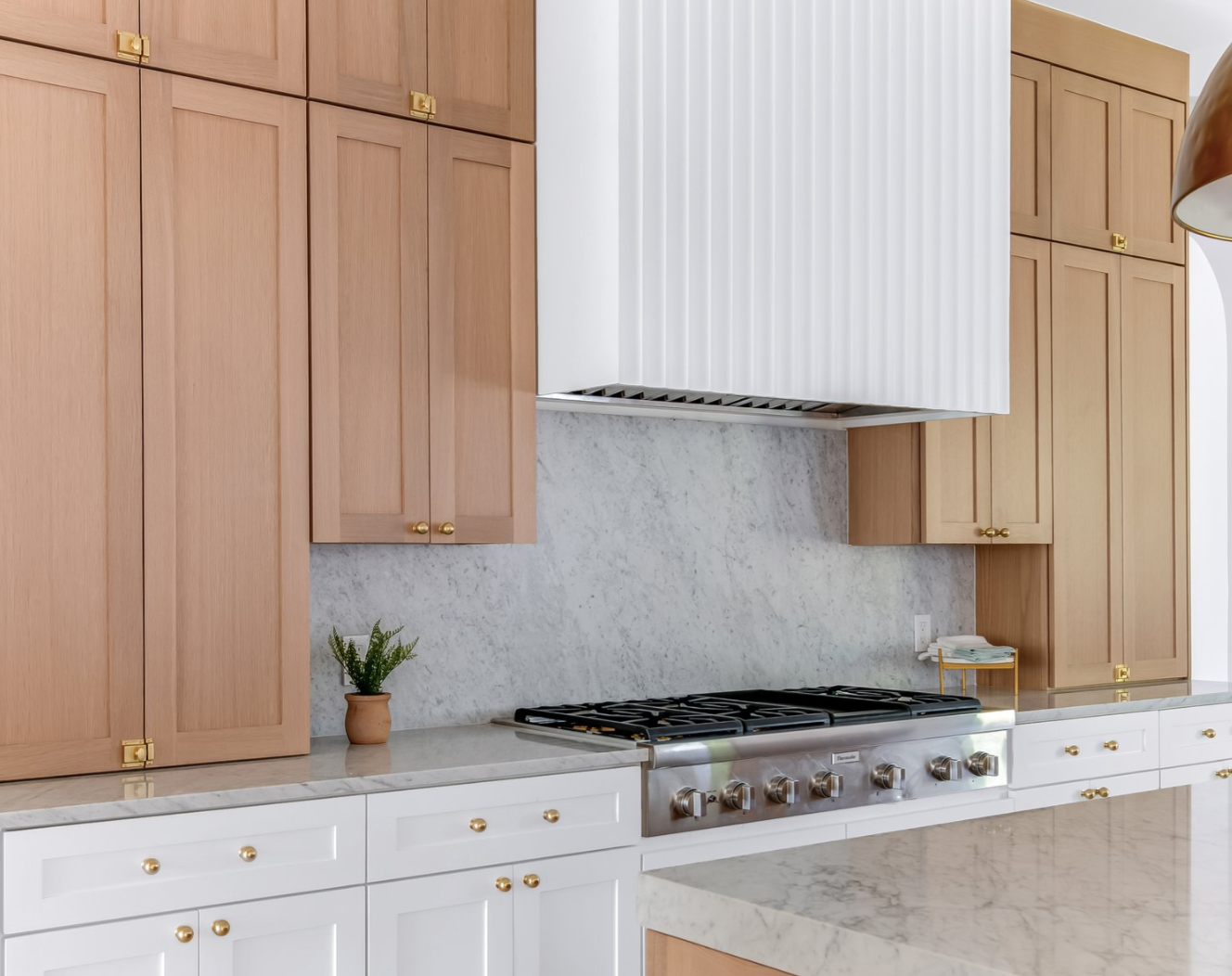 Kitchen with light wood and white cabinets, marble backsplash, range, and white range hood.