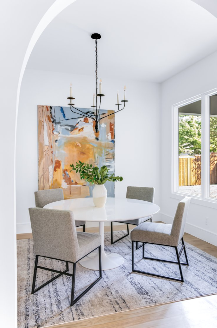 Dining room with white table, gray chairs, abstract art, and a black chandelier.