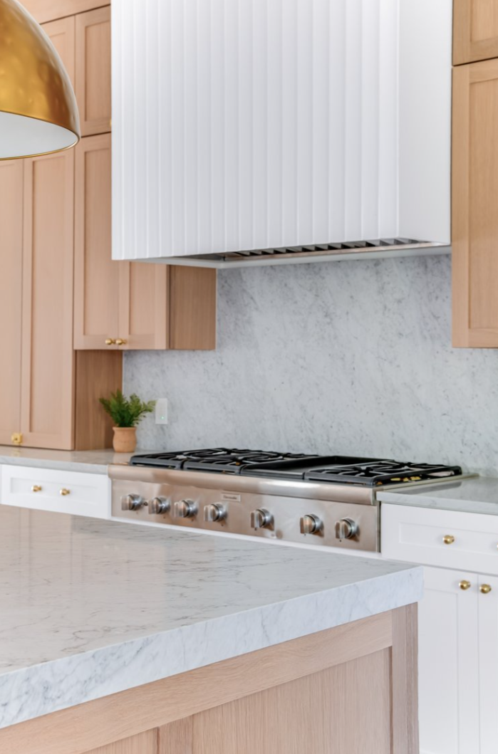 Modern kitchen with light wood cabinets, white marble backsplash, and stainless steel range.