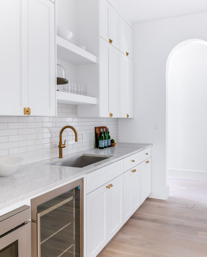 White kitchen with cabinets, sink, wine cooler, and gold accents.