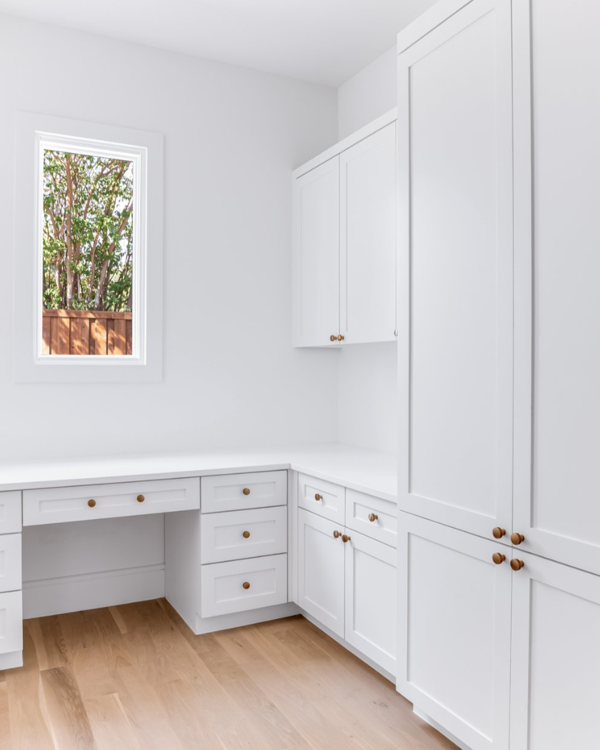 White home office with cabinets, desk, and window; hardwood floor.