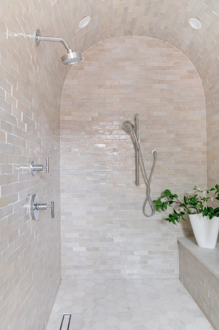 Shower with arched ceiling, beige tiled walls, and a bench with potted plant.