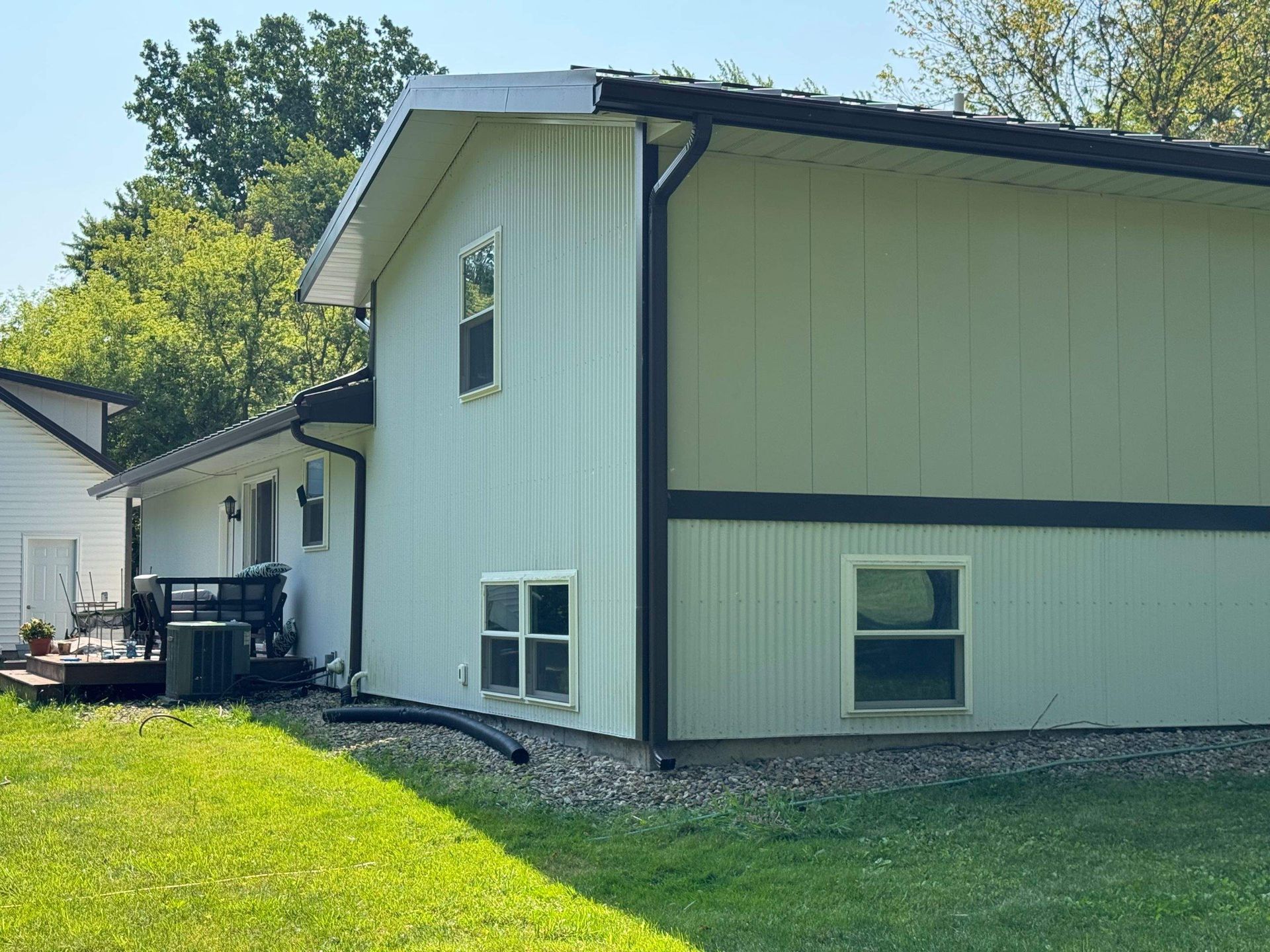 Side view of a light-colored house with dark trim, grassy yard, and trees in the background