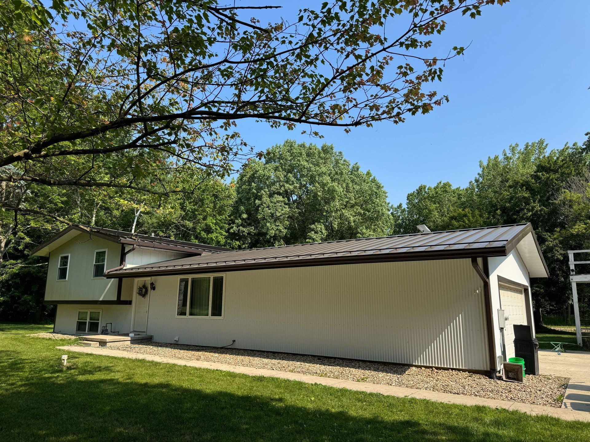 White house with a gray roof in a grassy yard, surrounded by trees on a sunny day