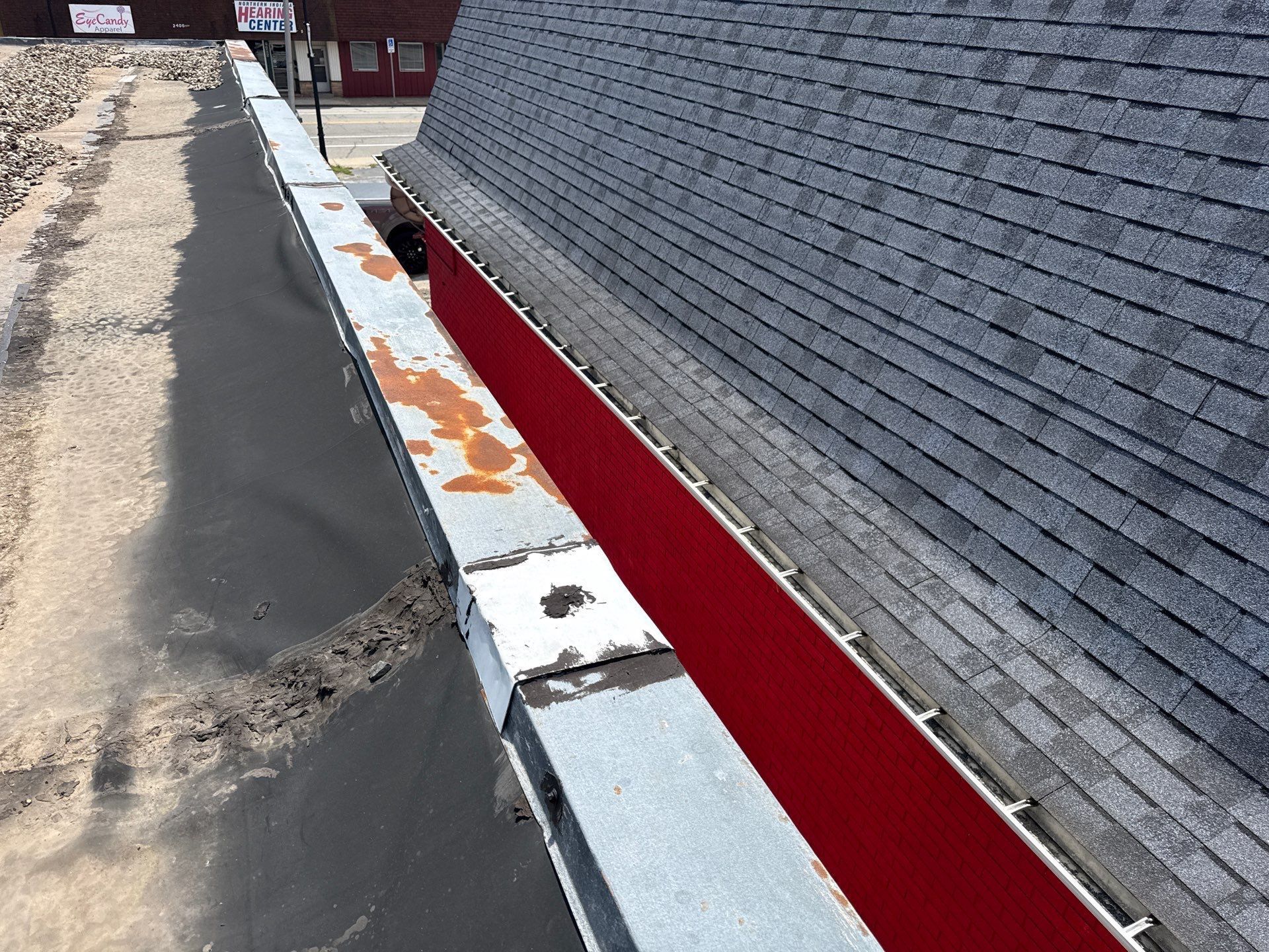Rooftop edge with red flashing and gray shingles beside a black paved walkway