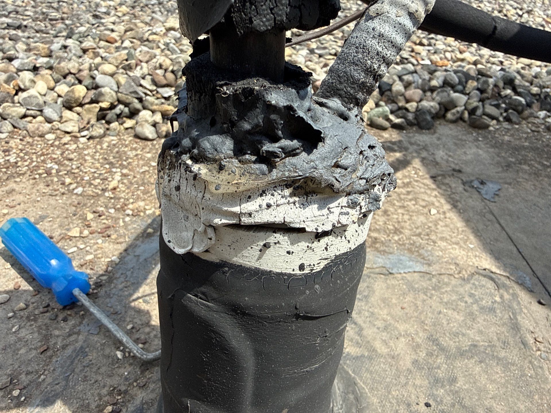 A charred black pipe with melted foam insulation on a concrete surface, with a blue screwdriver nearby.