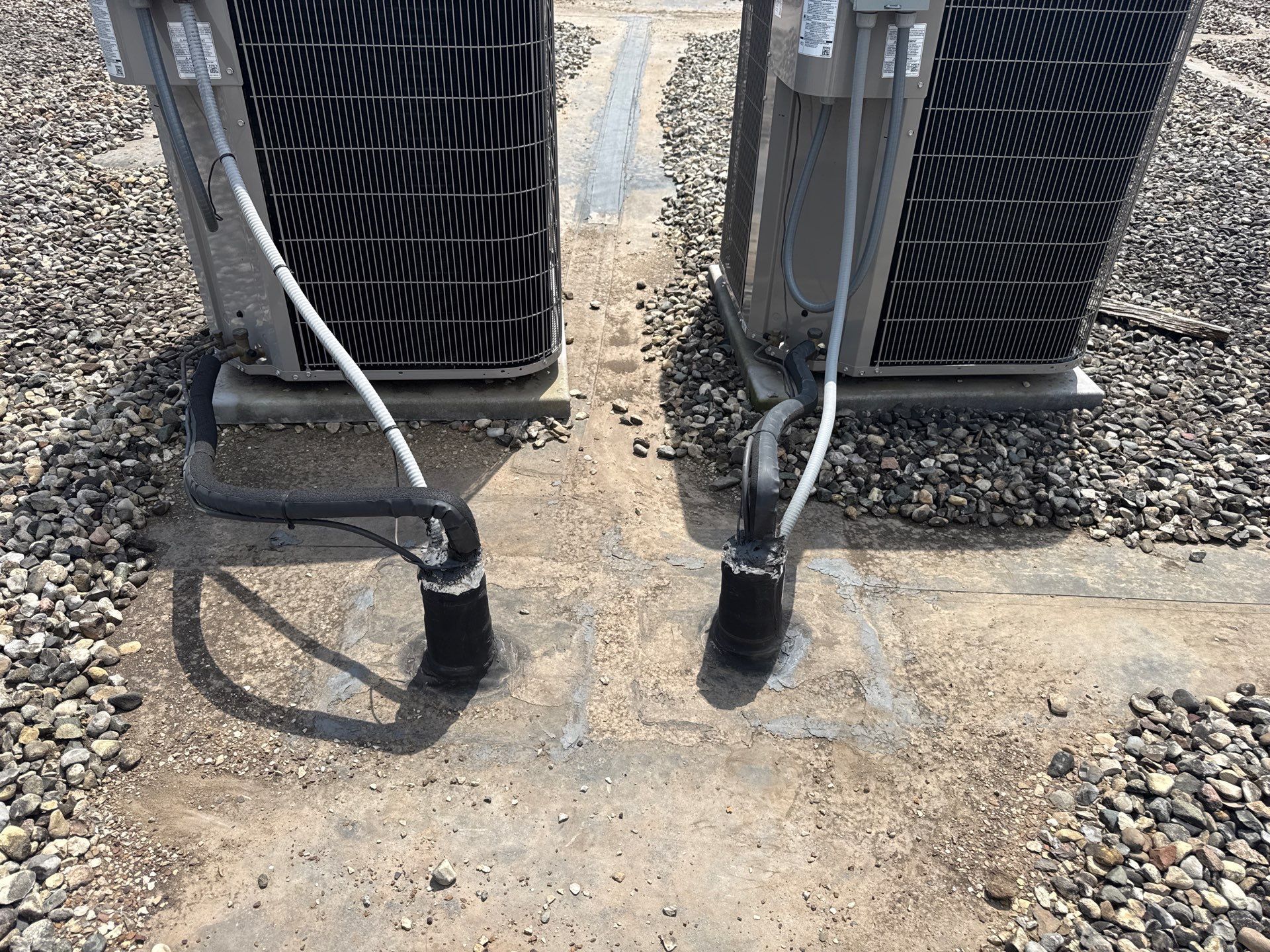 Two outdoor HVAC units with hoses on gravel, one shadowed by bright sunlight