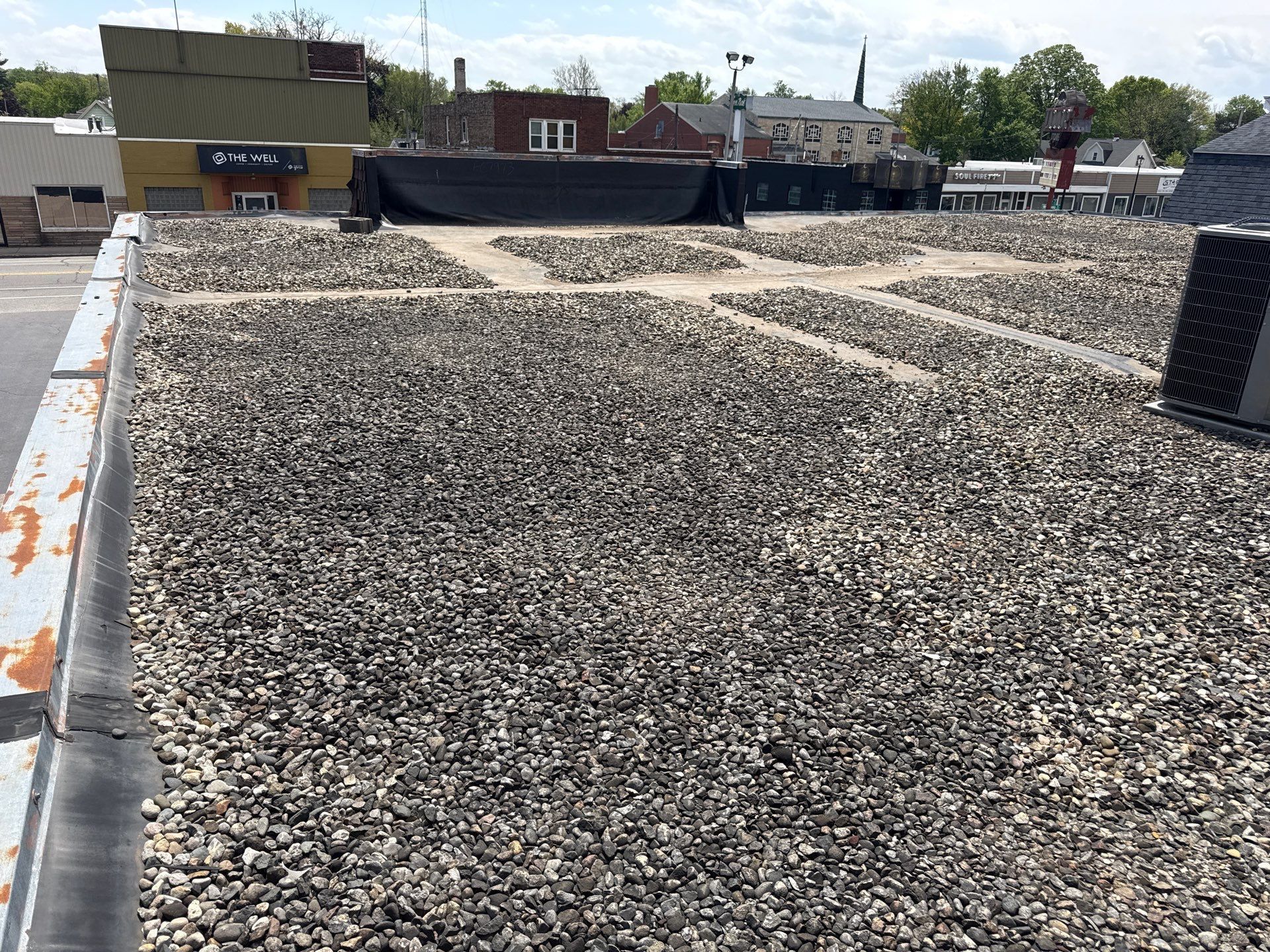 Gravel-covered rooftop with vents, parapet walls, and buildings in the background