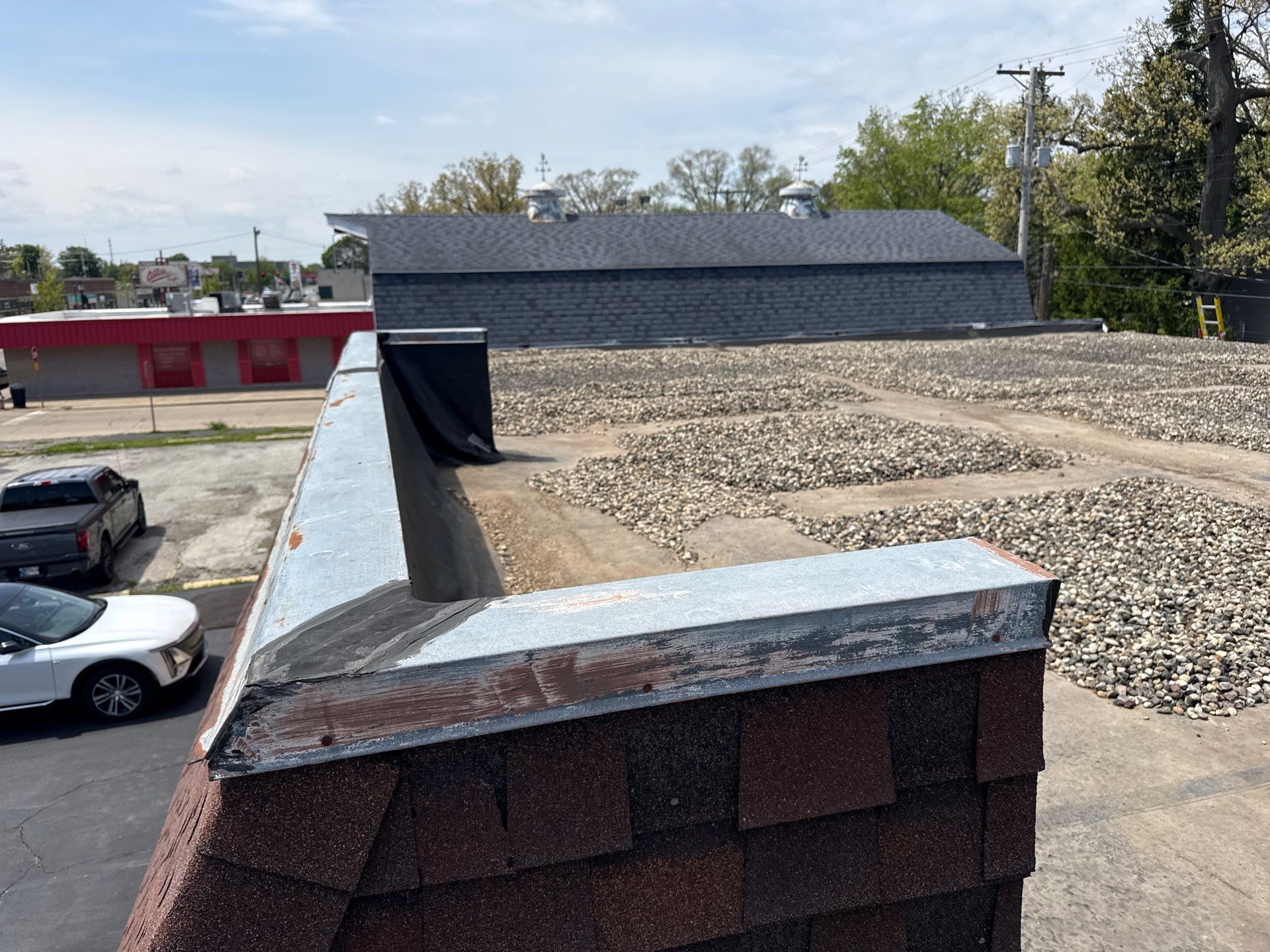 Flat rooftop with gravel, brick parapet, and HVAC units under a partly cloudy sky