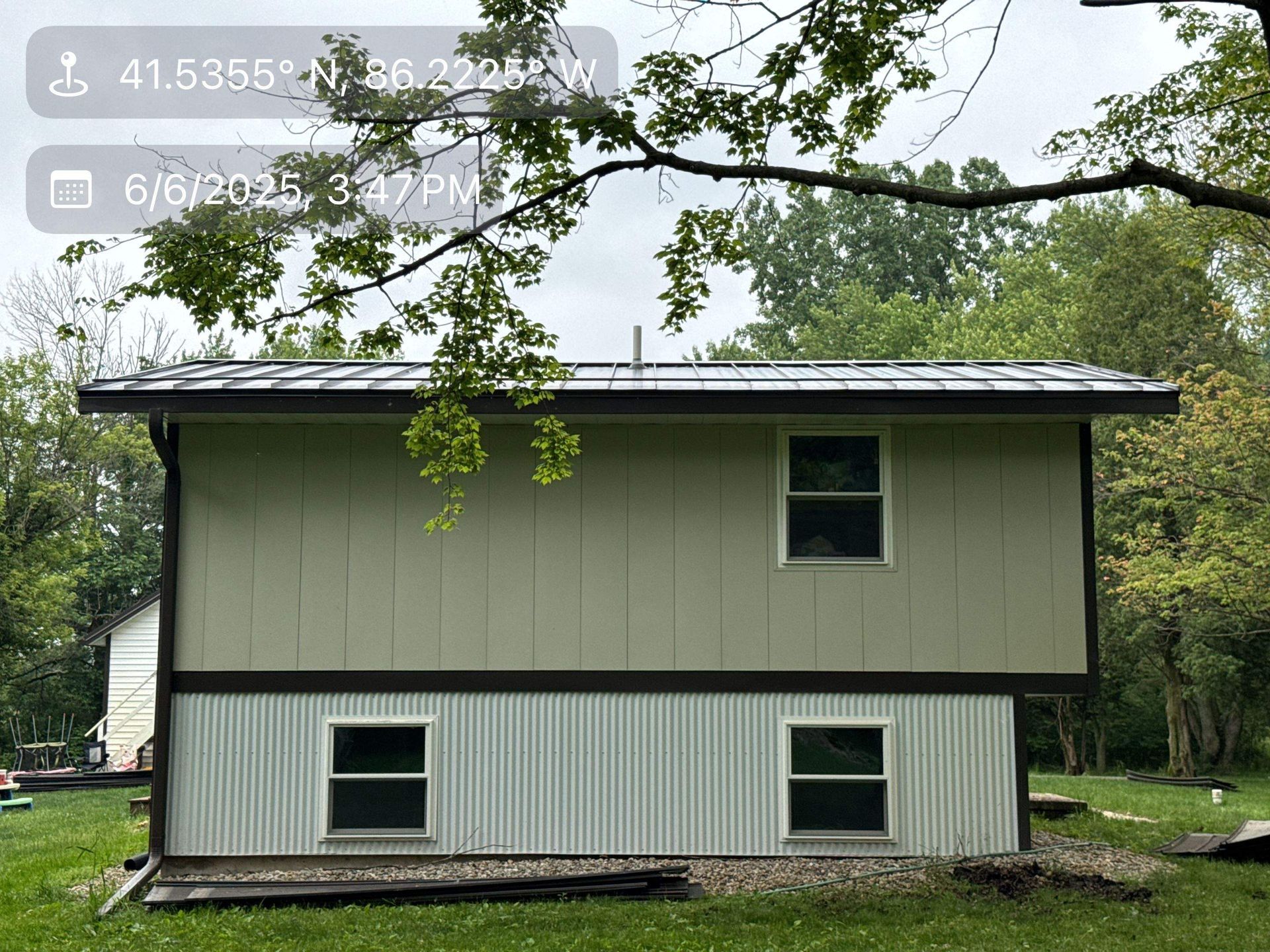 Two-story beige and white house with a dark roof, framed by trees in a wooded yard.