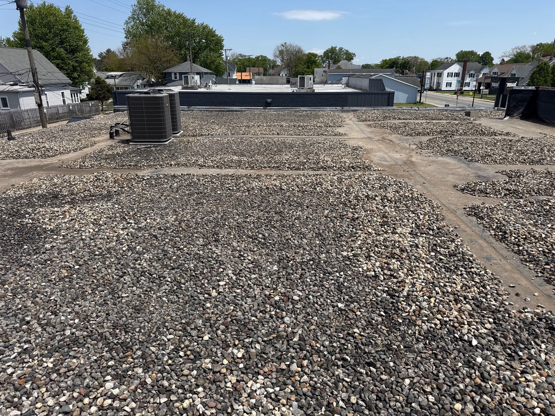 Gravel-covered construction site with concrete foundations, a trench, and trees in the background