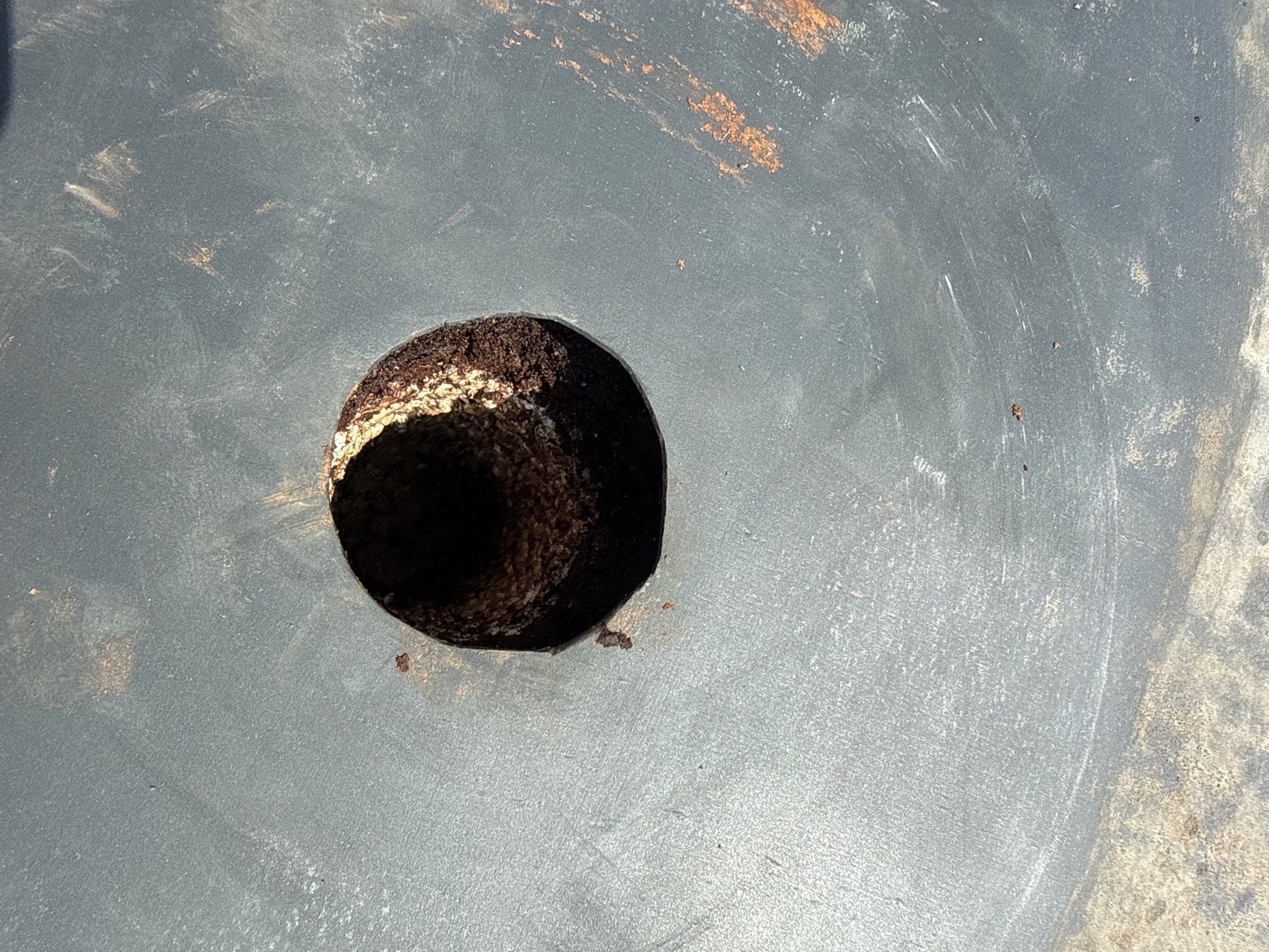 Close-up of a dark circular hole in a gray, slightly textured surface with orange specks