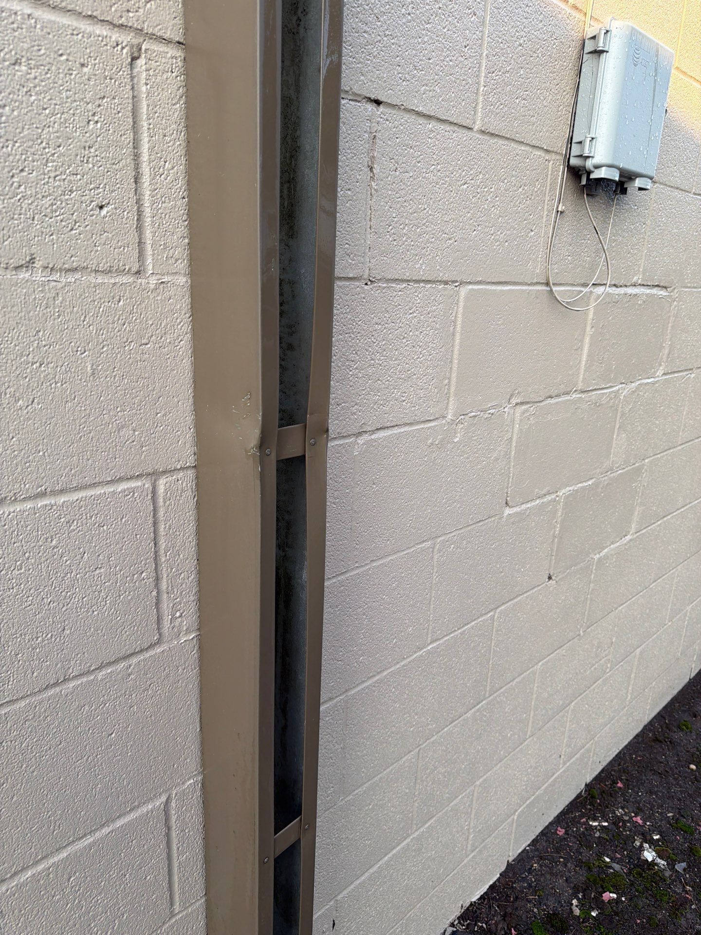 Close-up of a cinderblock wall with a narrow vertical gap and an electrical box mounted near the top.