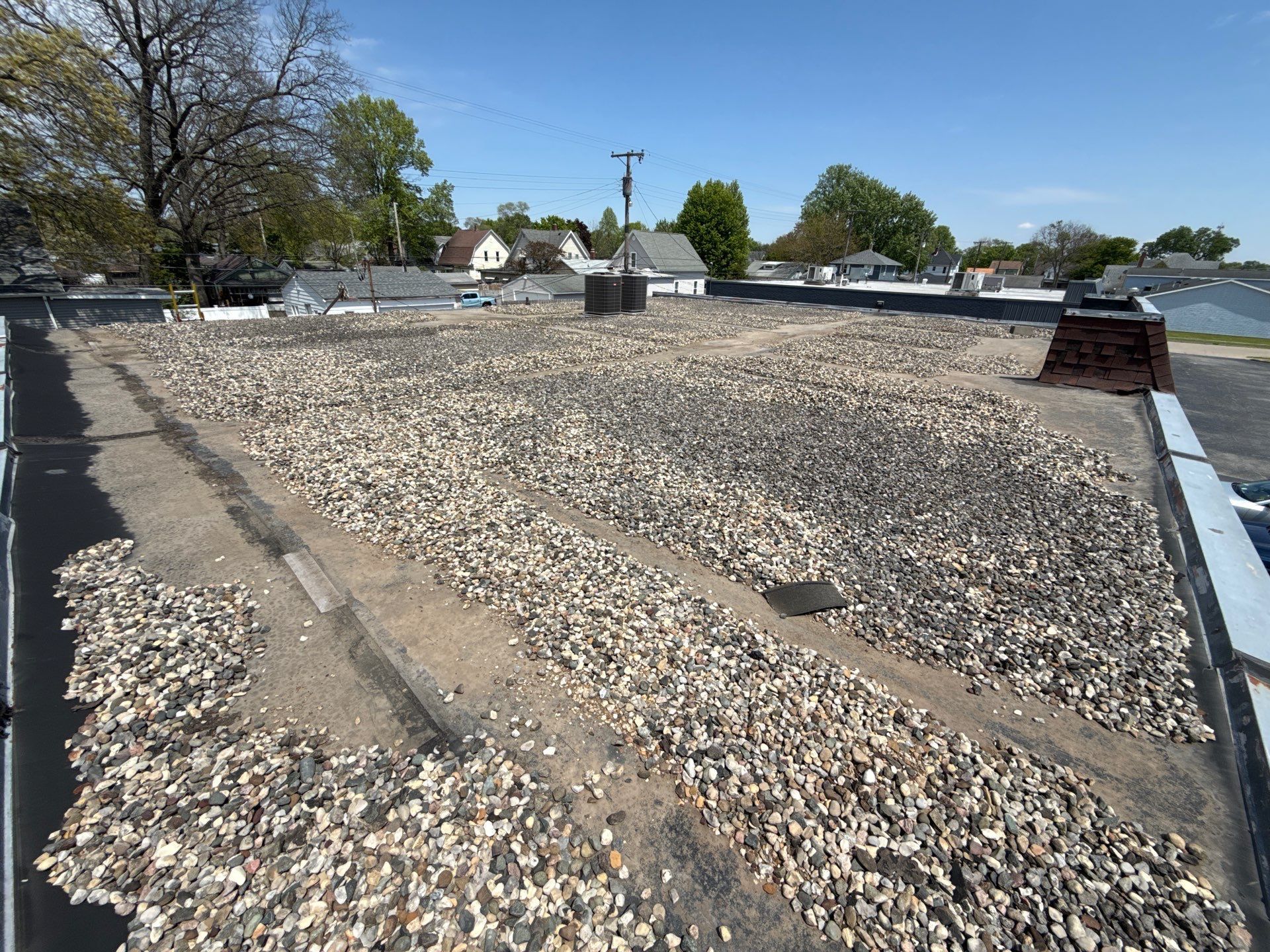 Flat rooftop covered with gravel, with trees and low buildings visible in the background