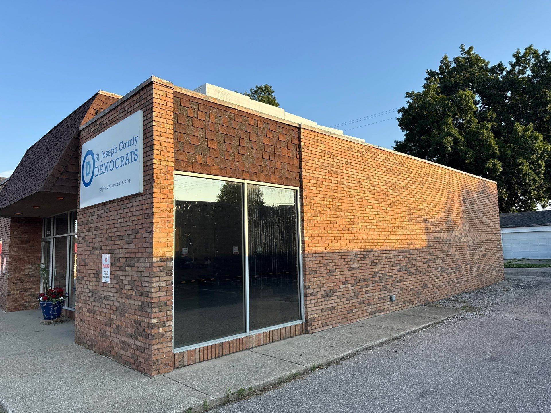 Brick commercial building with large dark windows and a sign, lit by sunlight on a gravel lot