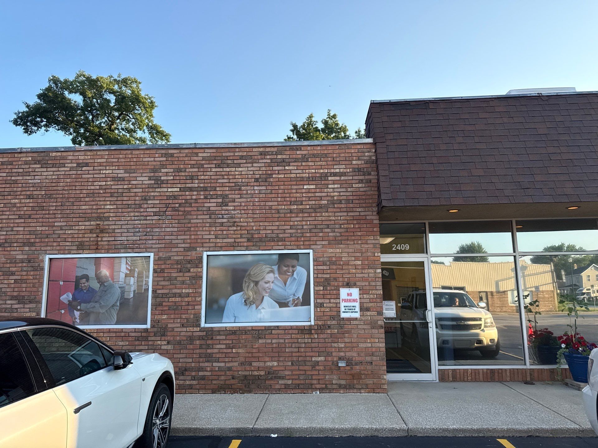 Brick storefront with two window posters, glass door, and a white car parked in front