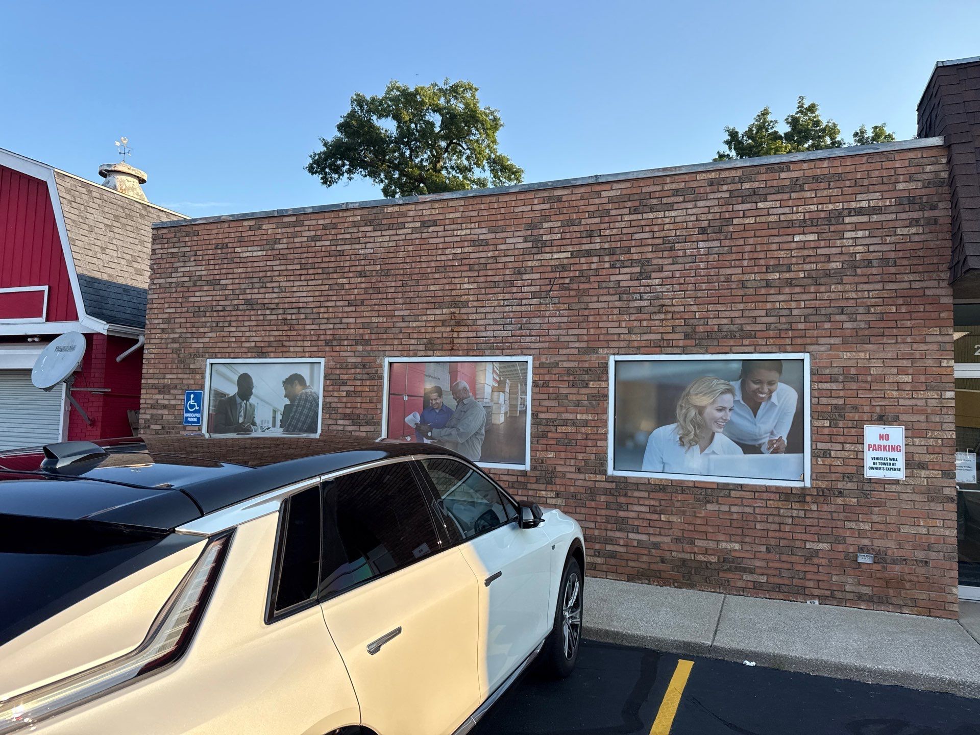 Brick building with three windows and posters, partially blocked by a black-and-white car parked in front