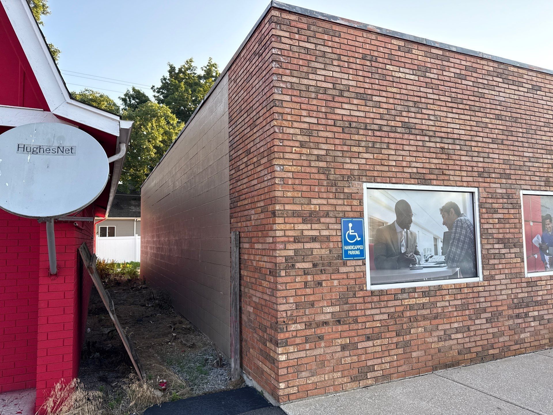 Brick building corner with accessibility sign and mural plaques beside a red structure