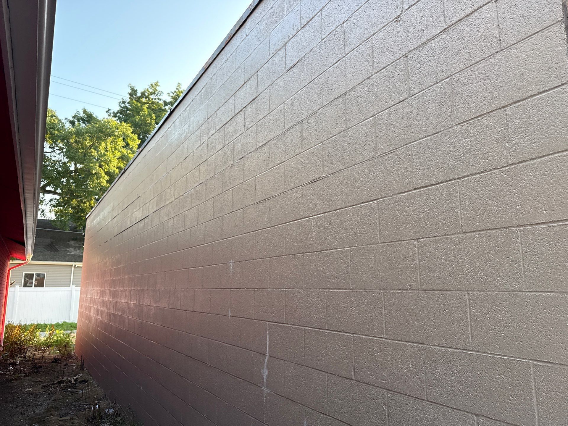 Long gray concrete wall beside a narrow outdoor passage, with sunlight and trees at the far end