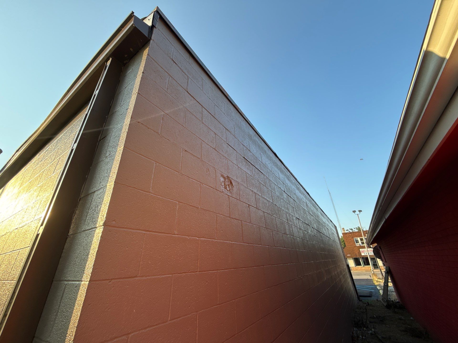 Narrow alley between red brick walls under a clear blue sky, viewed upward toward the opening.