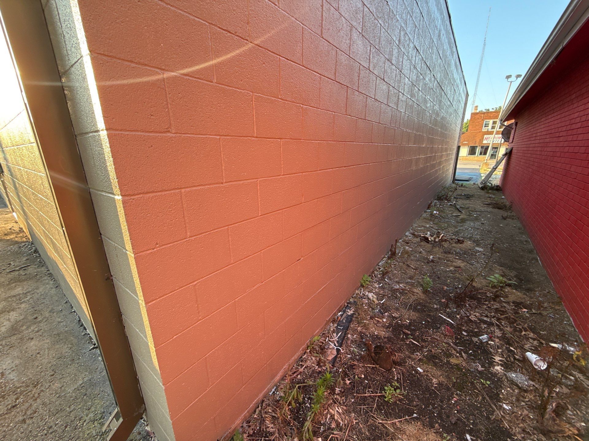 Narrow outdoor alley between red walls with muddy ground and bright sky at the end