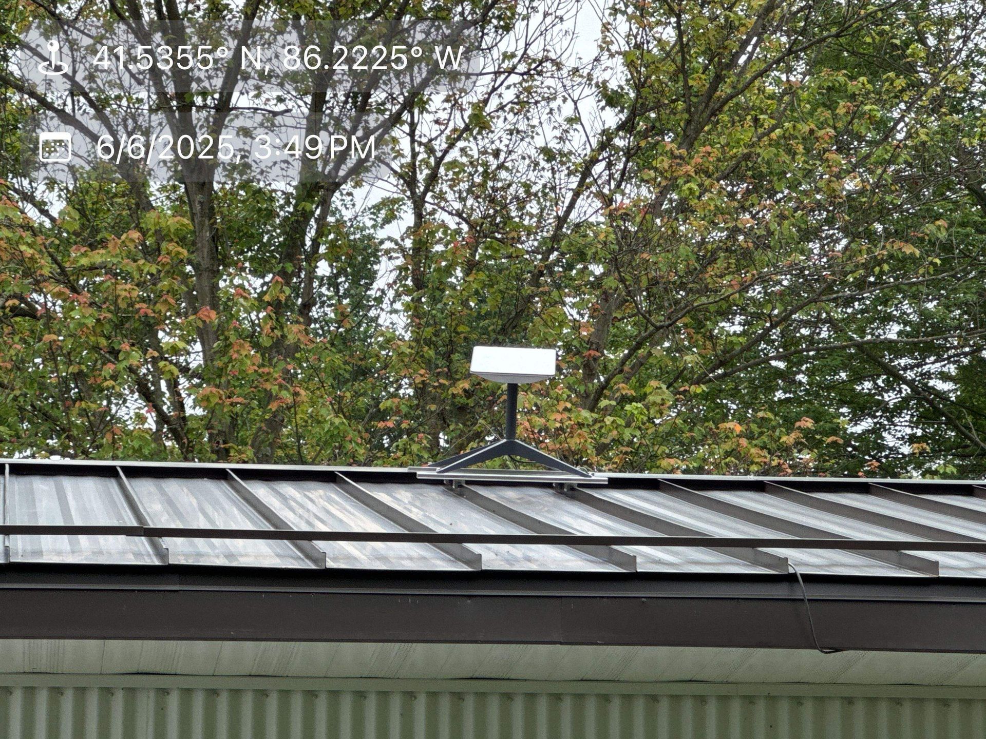 Rooftop with a small white antenna in front of leafy trees under a cloudy sky